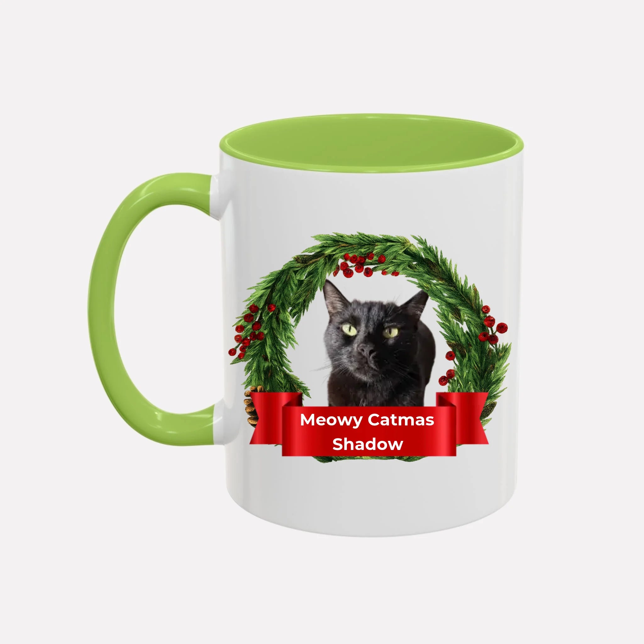 White sample mug with light green interior and handle, featuring a black cat in a Christmas wreath and 'Meowy Catmas Shadow' text.