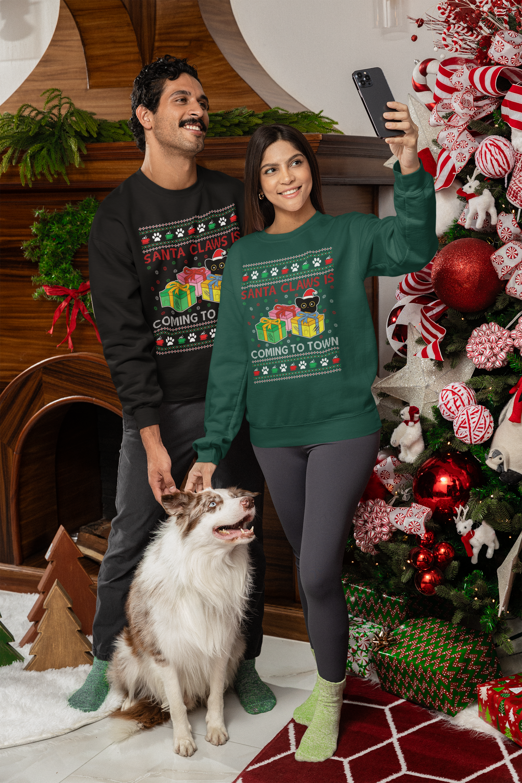 Man and woman in Purrcolate Ugly Pawliday sweatshirts with a dog. The man is wearing a Coal colored ugly sweatshirt and the woman is wearing an evergreen colored ugly sweatshirt. They are taking a selfie in front of a decorated Christmas tree.