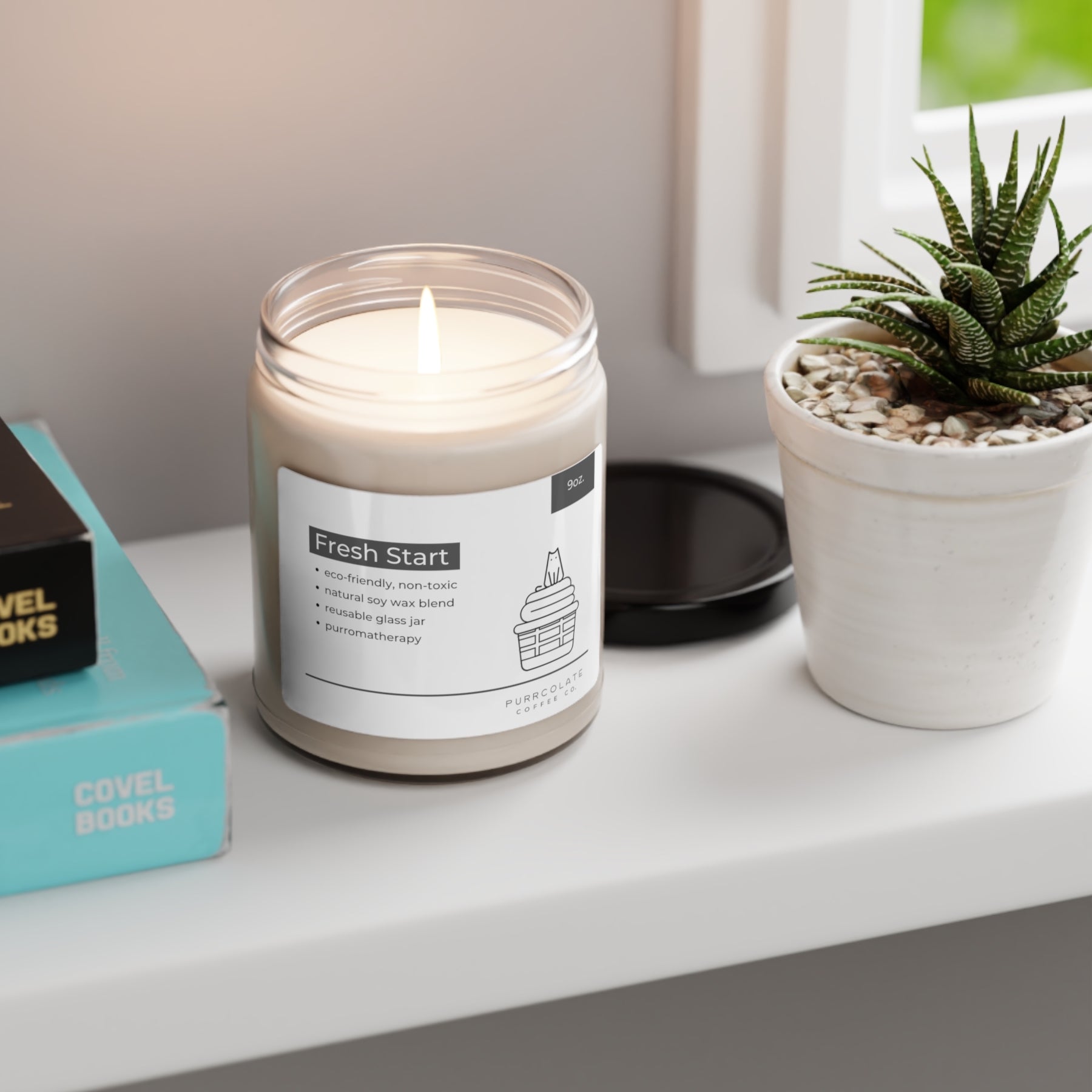 A Purromatherapy Soy Candle in the scent Fresh Start burns on a white desk next to a succulent plant and some books